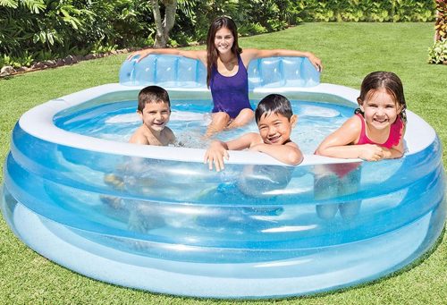 Four children are happily playing and lounging in a round, inflatable pool on a sunny day in a lush backyard.