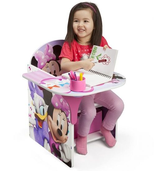 A little girl sitting in desk chair and show her drawing with smile